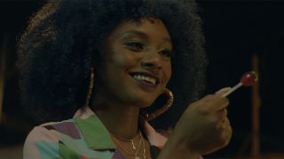 A beautiful Black woman with big curly hair and gold hoop earrings, smiling