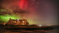 green and red auroras shine over a lit-up house at night