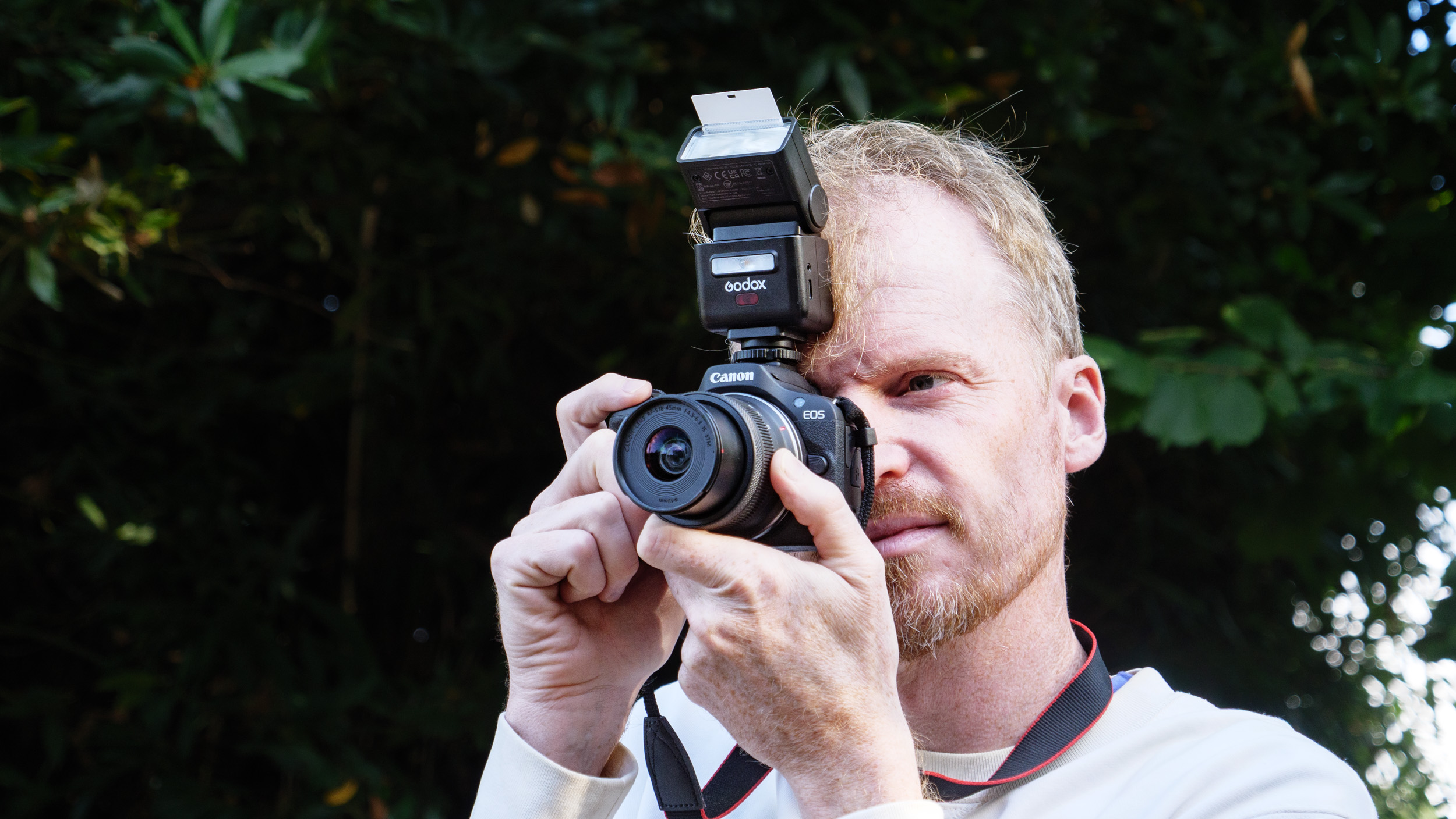 Photographer and TechRadar's Cameras Editor Tim Coleman holding a Canon camera up to his eye, there's a Godox iT32 camera flash attached to the camera