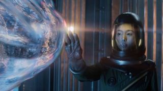 a woman in a spacesuit reaches out to touch a shimmery blob