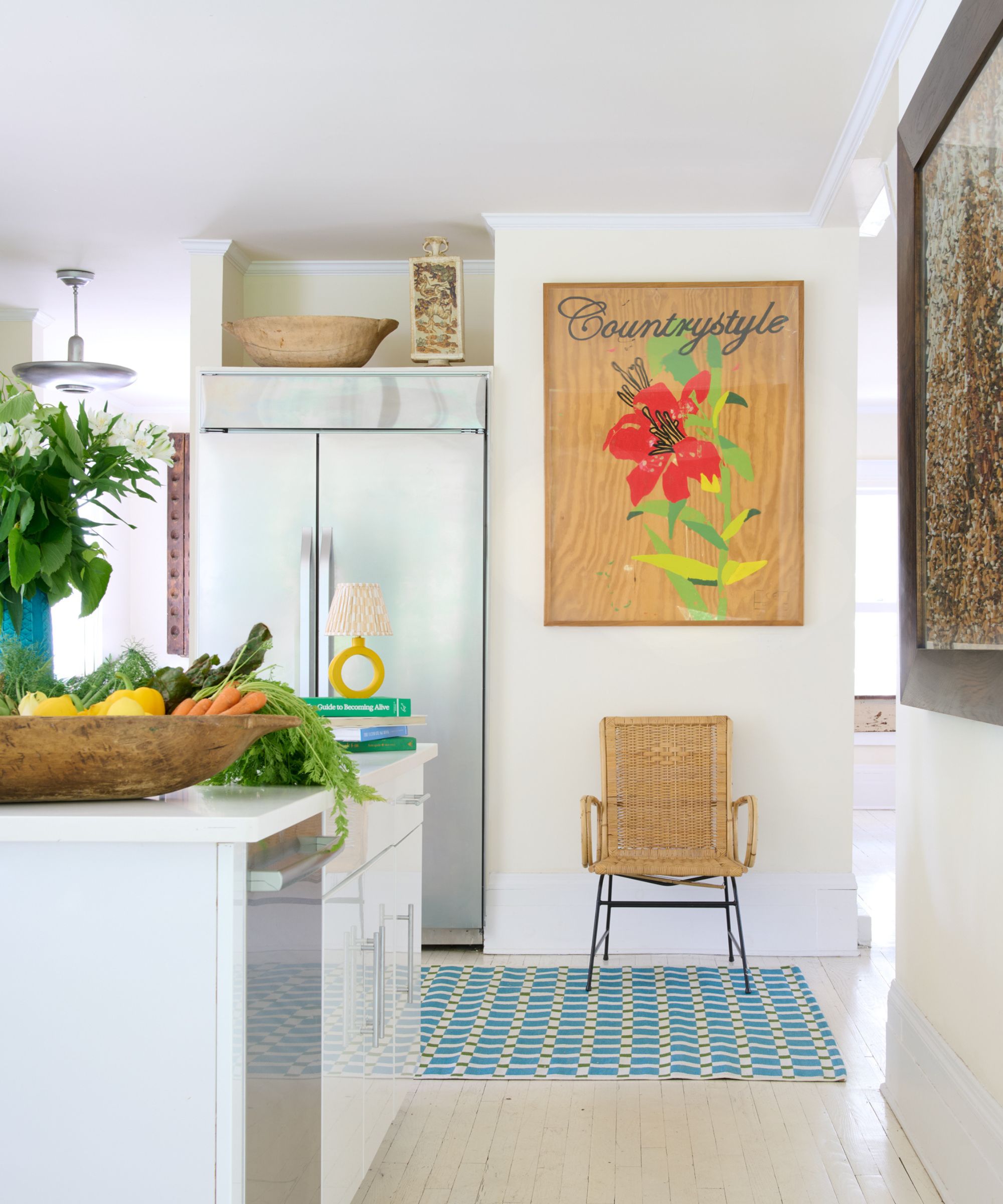 white kitchen with blue and yellow rug, rattan chair and colorful artwork