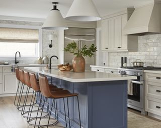 A large kitchen with navy blue island, greige cabinets and marble-tiles walls