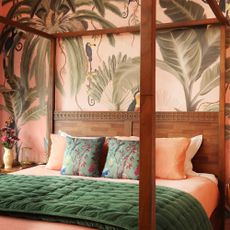A bedroom with a four poster bed and the walls covered in a peach-coloured wallpaper with a tropical print