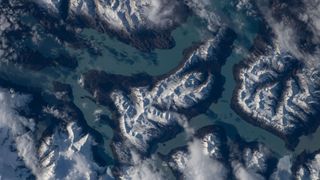An aerial image of snowy mountains and blueish-greenish water. 