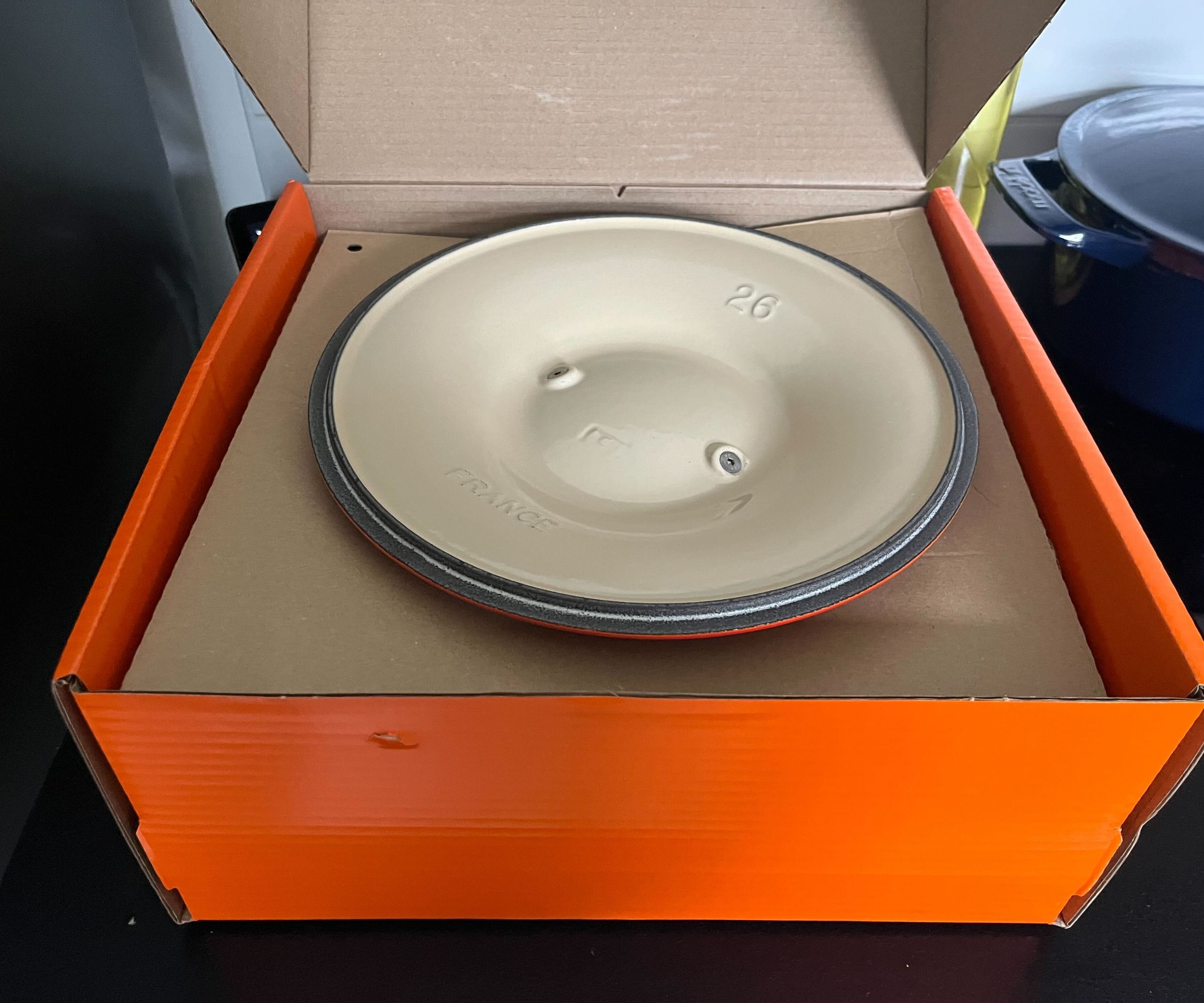 The open orange Le Creuset box with an upside down Dutch oven lid visible