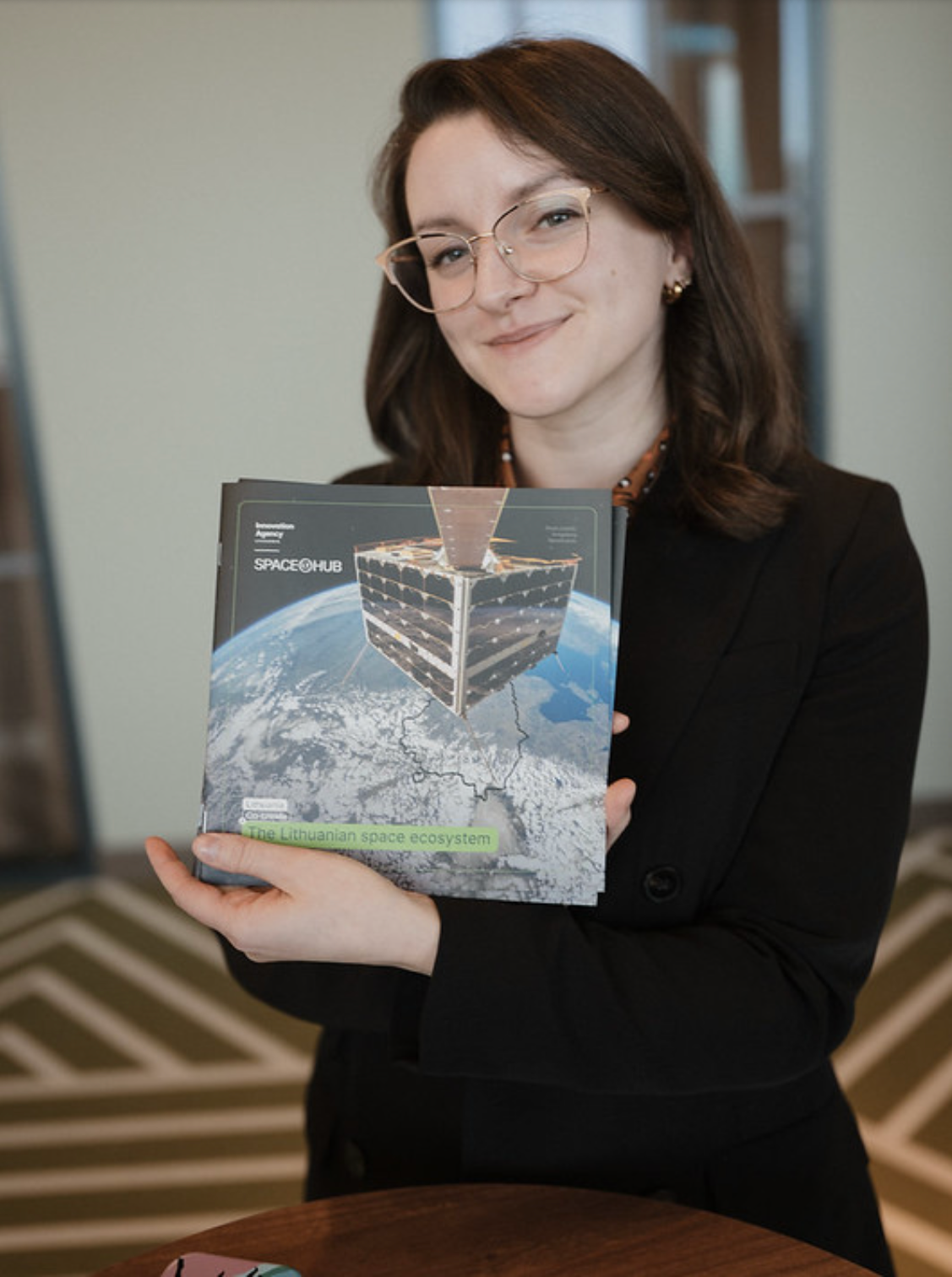 A woman with brown hair and glasses holding a booklet that says SpaceHub.