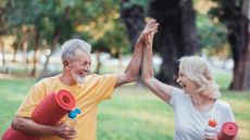 Senior Woman and Her Husband High Five As They Walk With Yoga Mats in the Park