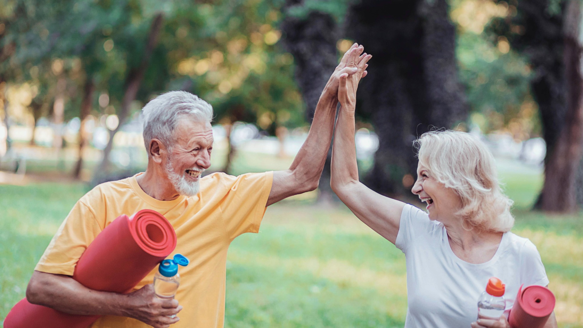 Senior Woman and Her Husband High Five As They Walk With Yoga Mats in the Park