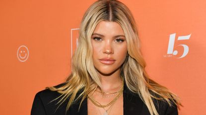 sofia richie in a black blazer at an event on the red carpet with an orange background