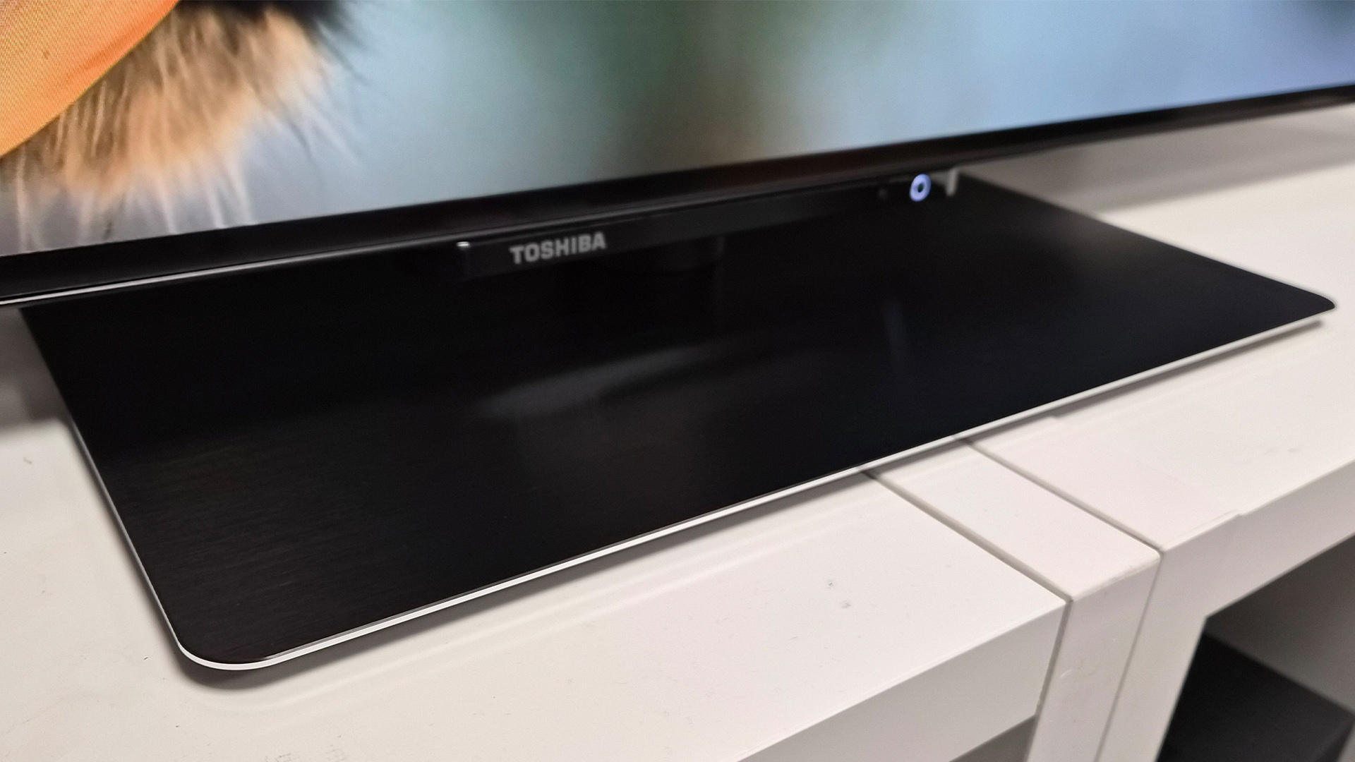 Toshiba XF9F OLED TV on white shelving unit detail of pedestal stand and Toshiba logo