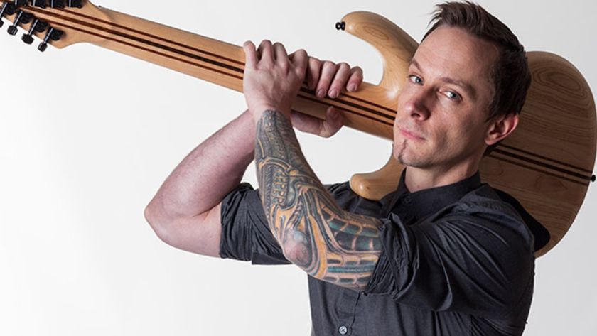 Composer Mick Gordon looking at camera while holding a guitar over his shoulder like a weapon.