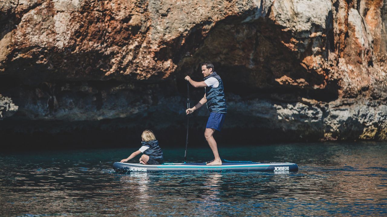 Best inflatable paddle boards: Man paddling a Jobe Infinity Seine 10.6 Inflatable Paddle Board with child sat on the front