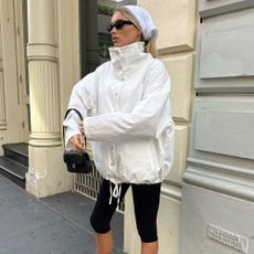 Elsa Hosk wears black capri pants with black heeled flip-flops and a white high-neck jacket.
