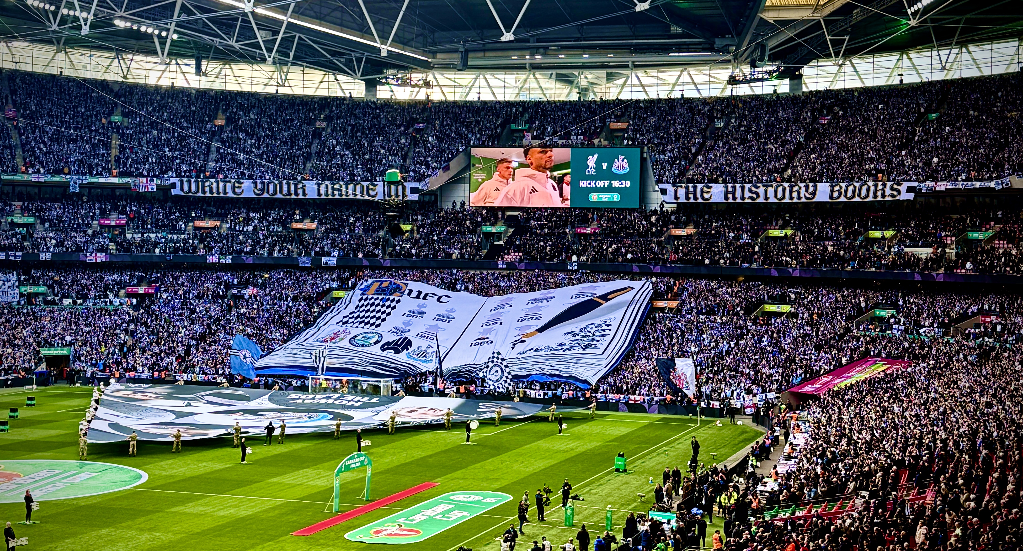 Newcastle United fans unveil a TIFO display curated by supporter group Wor Flags that says 'Write Your Name In The History Books' and features a quill and book. Image taken by journalist Matthew Ketchell