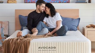 A couple laugh and cuddle while sat on the Avocado Eco Organic Mattress