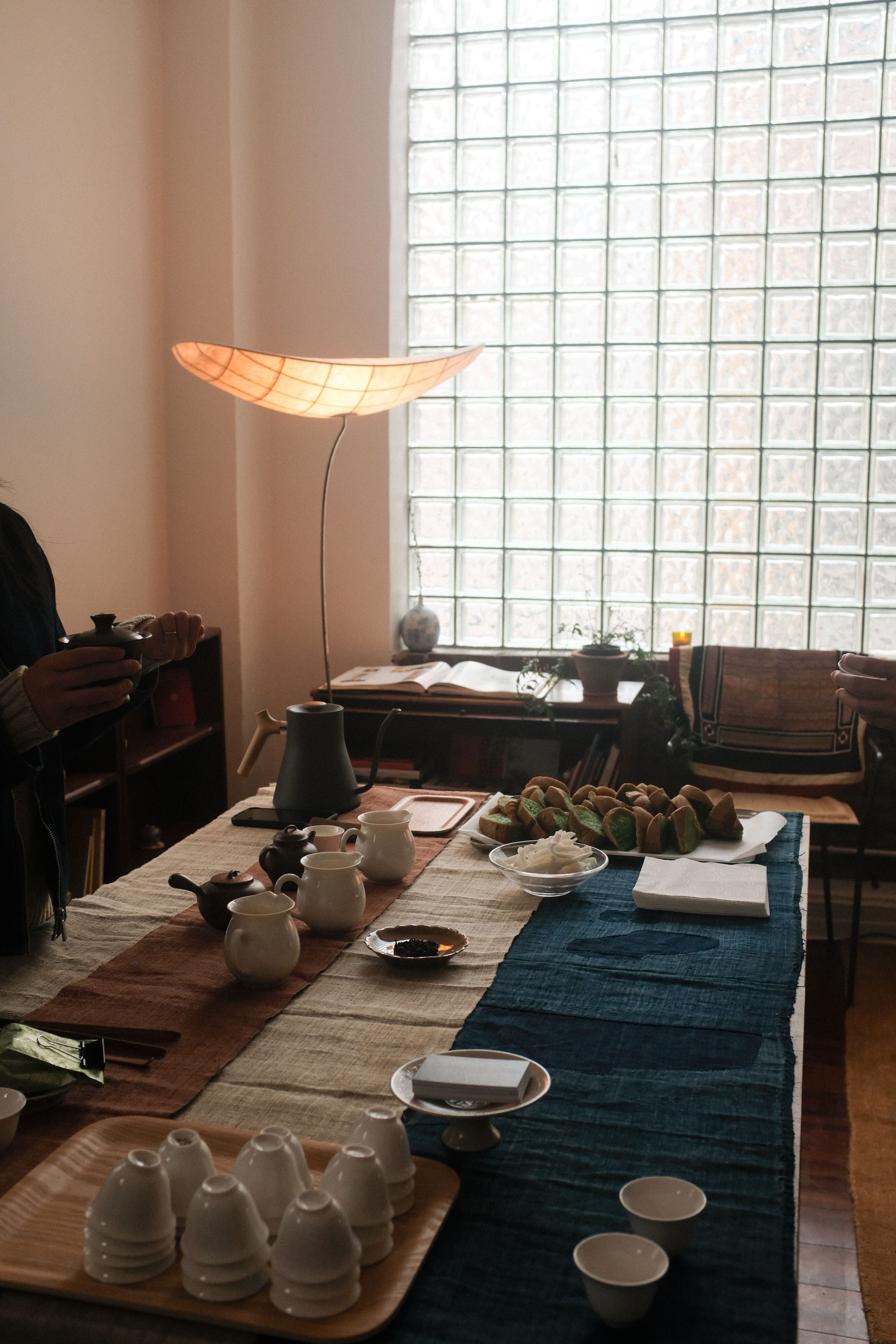 A traditional Vietnamese tea time setup, with ceramic mugs, slices of cakes, and a leaf blend all positioned atop a Vietnamese flag in a naturally lit gallery.