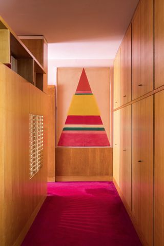 Passage way with wooden cupboards, pink carpet and triangular painting on the end wall.