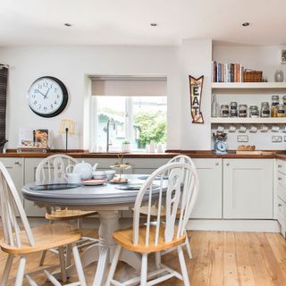 White kitchen with round grey painted table and four white chairs