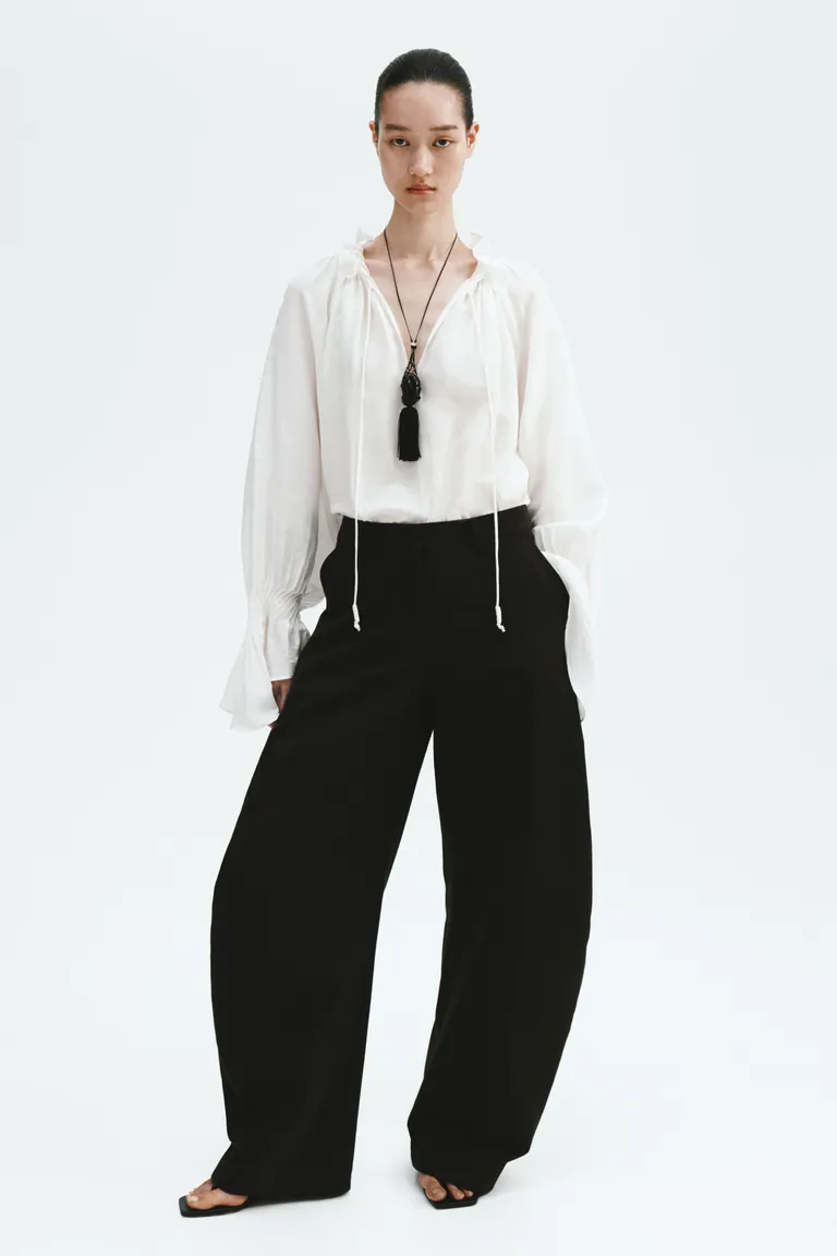 Model wears white blouse, black trousers and necklace