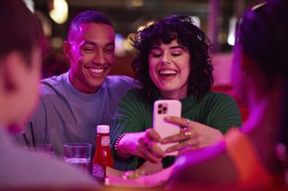 Two people take a selfie on an iPhone in a crowded bar