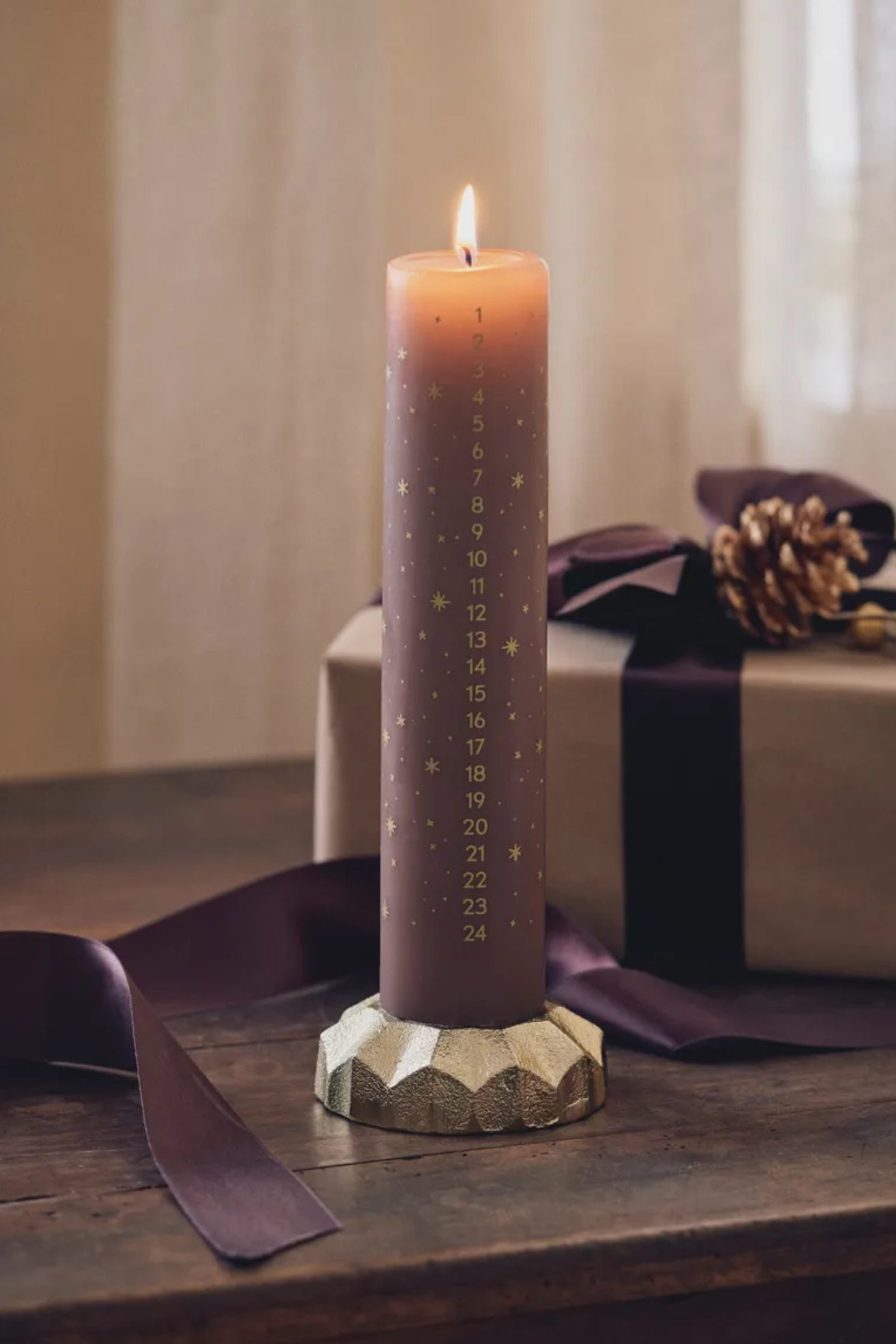 A mocha colored advent candle with gold etchings on a holder