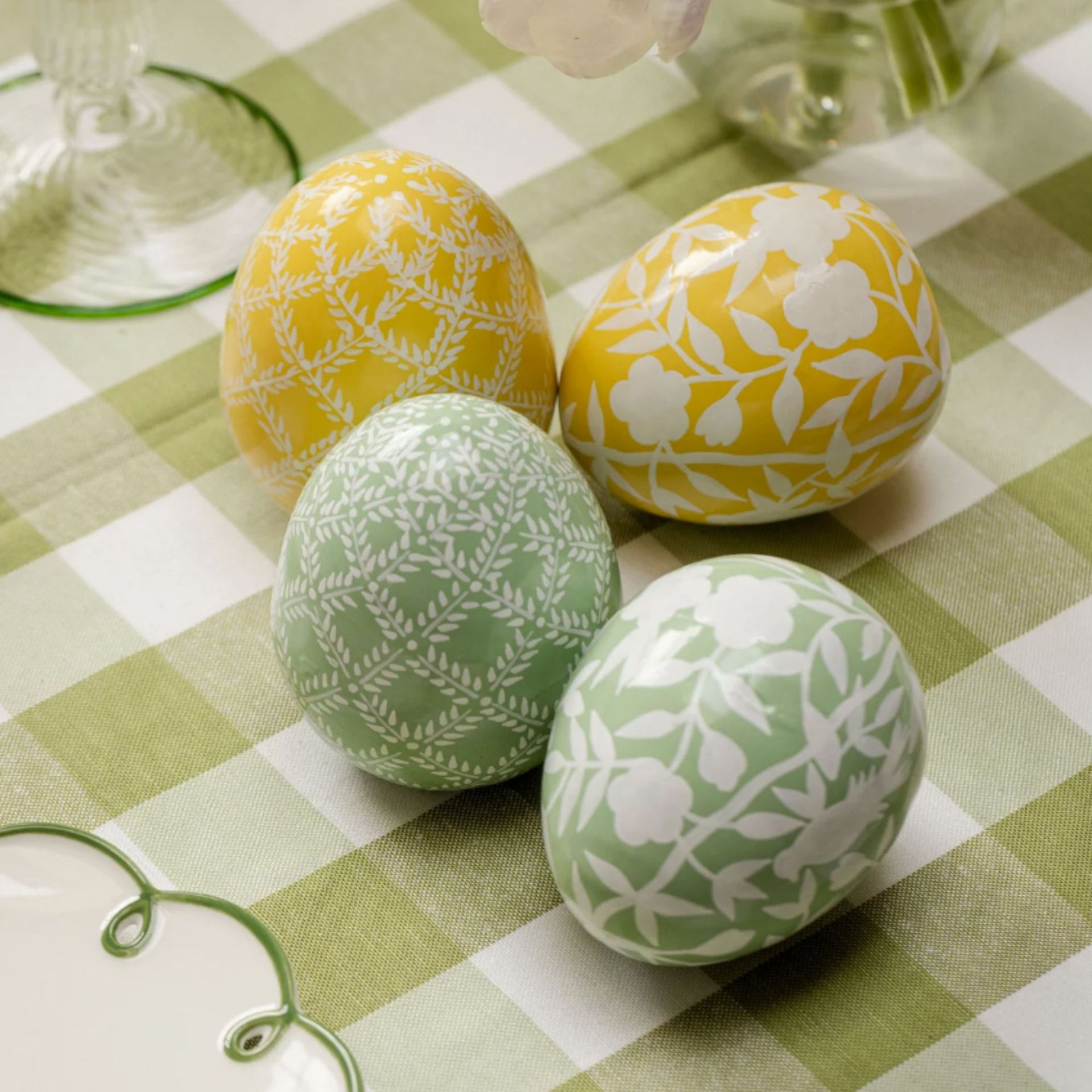 Hand painted easter egg decorations in green and yellow with floral motifs on a green gingham tablecloth
