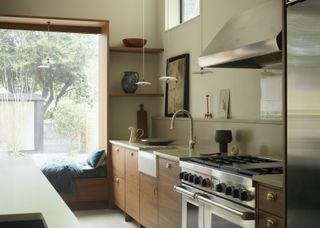 A kitchen extension with window seating/ a window bench. The kitchen has a kitchen island, as well as countertops. Above the countertops are three pendant lights.