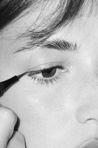 Close up black and white image of lady doing eyeliner