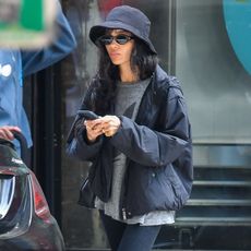 Zoe kravitz wears a black hat, gray t shirt, black jacket, black pedal pusher leggings, and black flats.