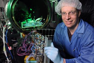 The U.S. Naval Research Laboratory’s Paul Jaffe holds a module designed for space solar power investigations in front of a customized vacuum chamber used to test the device.