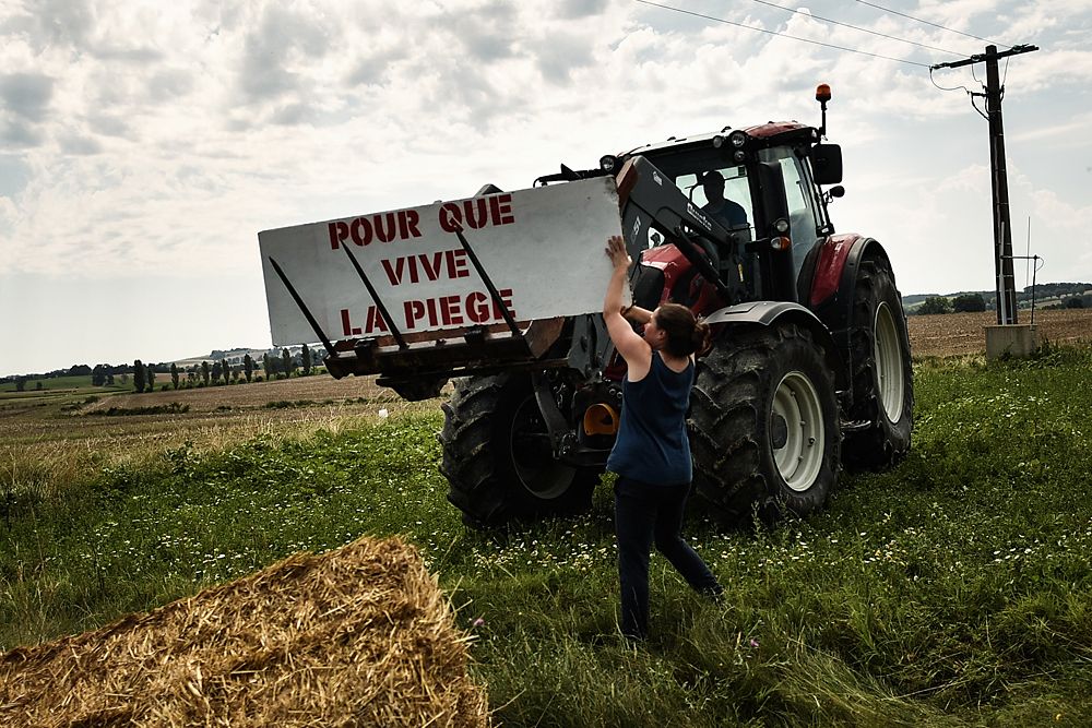 A protester holds a placard reading 'For the Piege region to live' as gendarmes stand watch (Rear) during a farmers' protest who attempted to block the stage's route