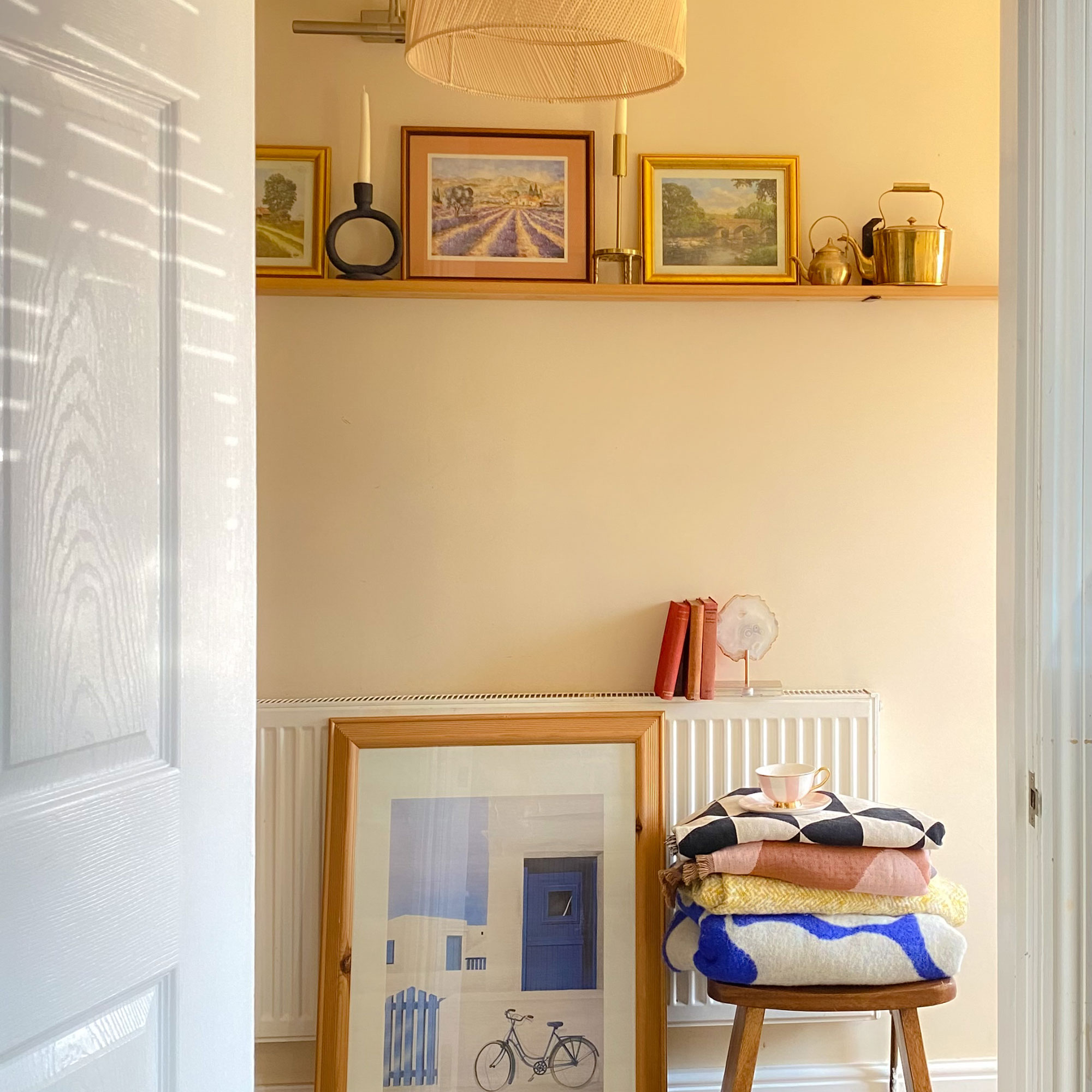 Neutral room with artwork leaning against radiator and decorating floating shelf above, alongside candles and ornaments