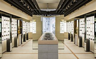 An eye glasses store with various types of glasses displayed on wall shelves and an island in the middle of the room with stones on top of it and a large mirror behind it.