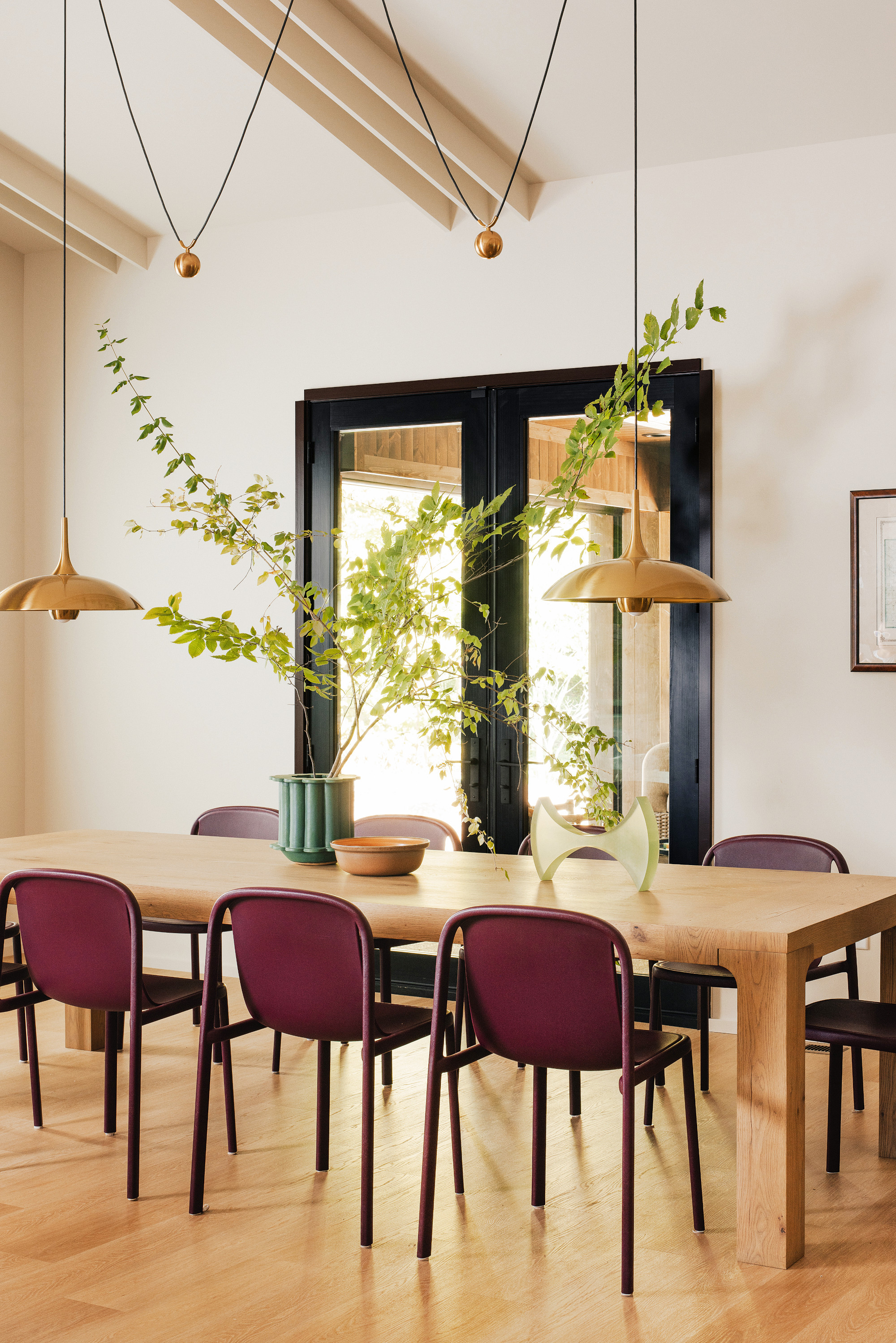 Off-white dining room with long rectangular wooden dining table, burgundy chairs and brass pendant lights