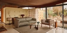 A earthy-shaded series of stripy mid-century modern furnishings sits in a desert house with floor-to-ceiling windows.