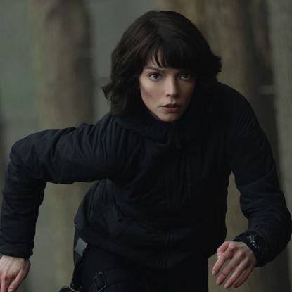 anya taylor joy in an all black outfit running through a forest in a still from the thriller the gorge