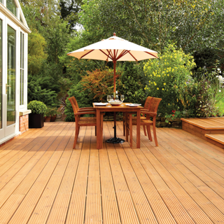 Oiled decking with wooden table and chairs and parasol in front of trees and plants