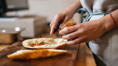 Hands spreading a condiment in a cut-open pita with a knife