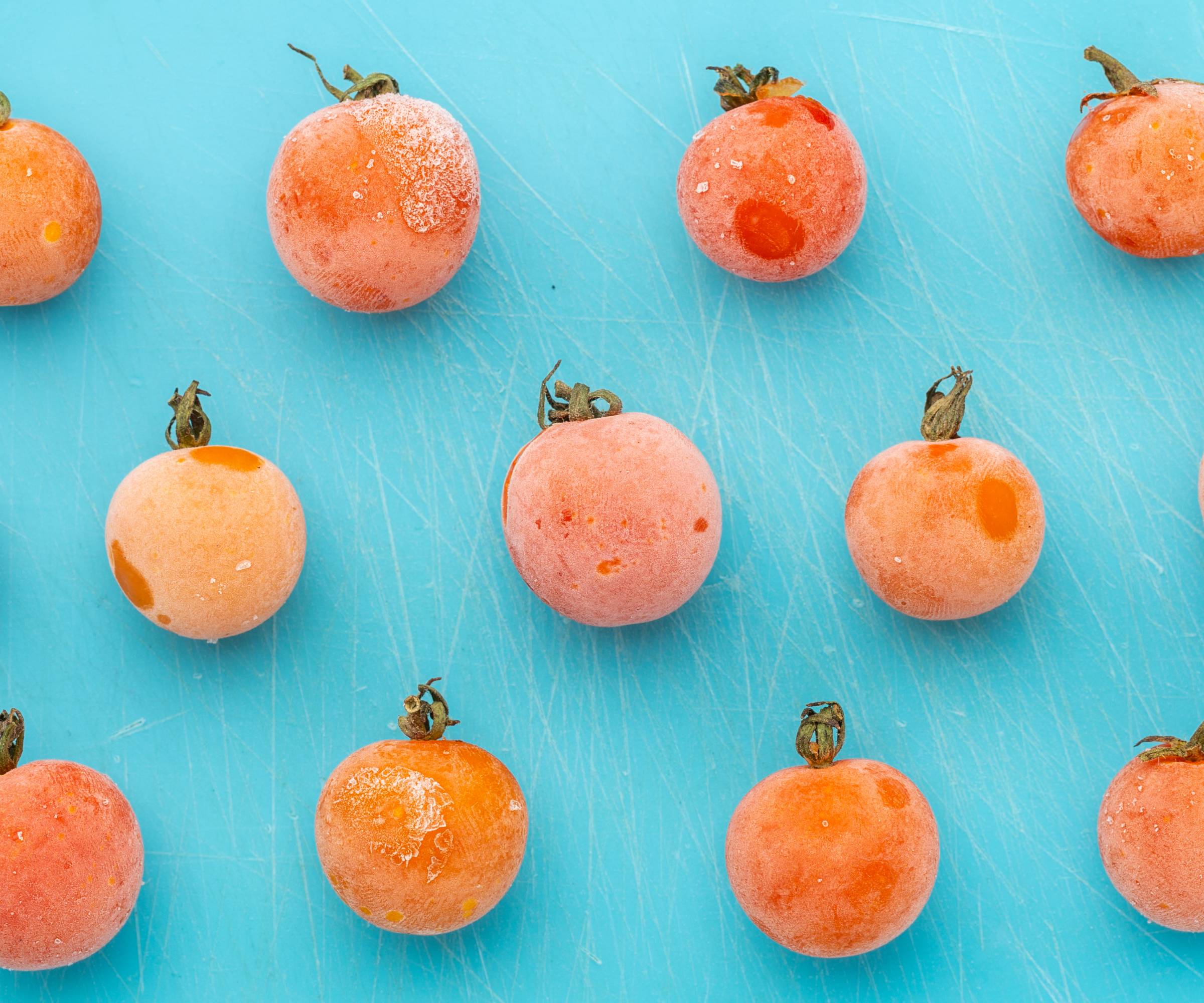 Frozen yellow cherry tomatoes on a teal background