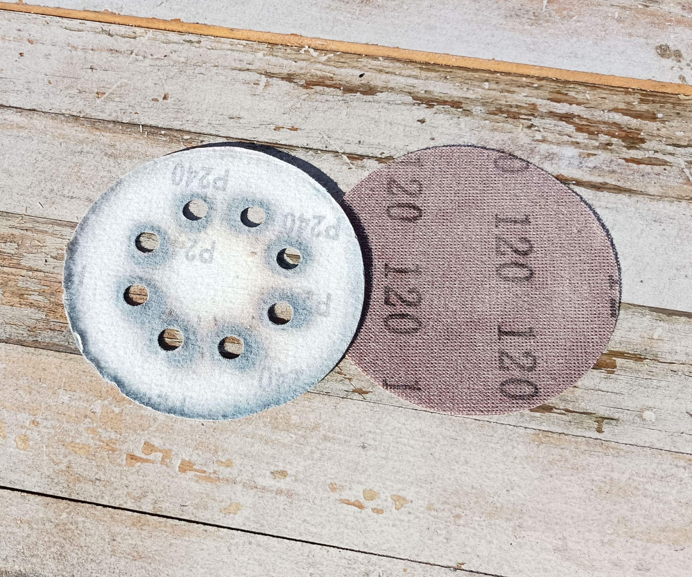 Two sandpaper discs with P number on display on whitewashed wood background