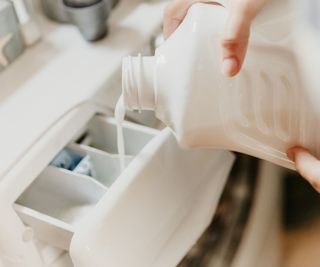 Someone pouring liquid laundry detergent into a drawer