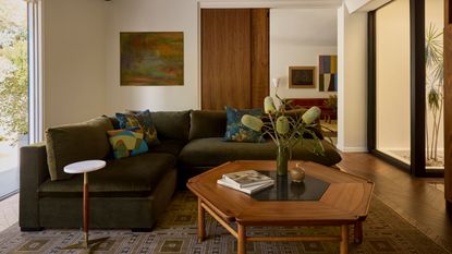 Living room with olive green velvet corner sofa, hexagonal wood coffee table with large foliage in vase
