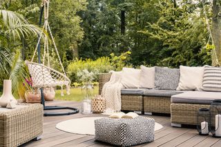 A modern, boho chic patio with a rattan corner sofa covered in lots of soft furnishings.