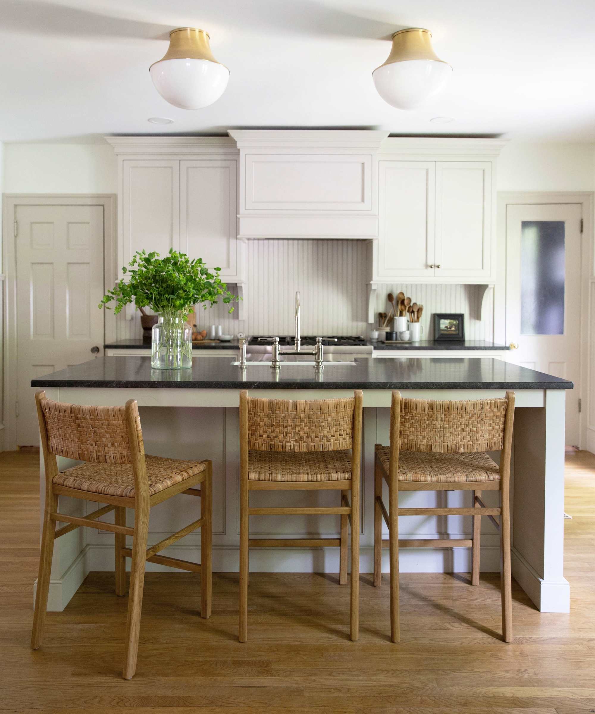 A neutral kitchen painted in Benjamin Moore's revere Pewter, paired with black countertops and natural woven wood bar stools