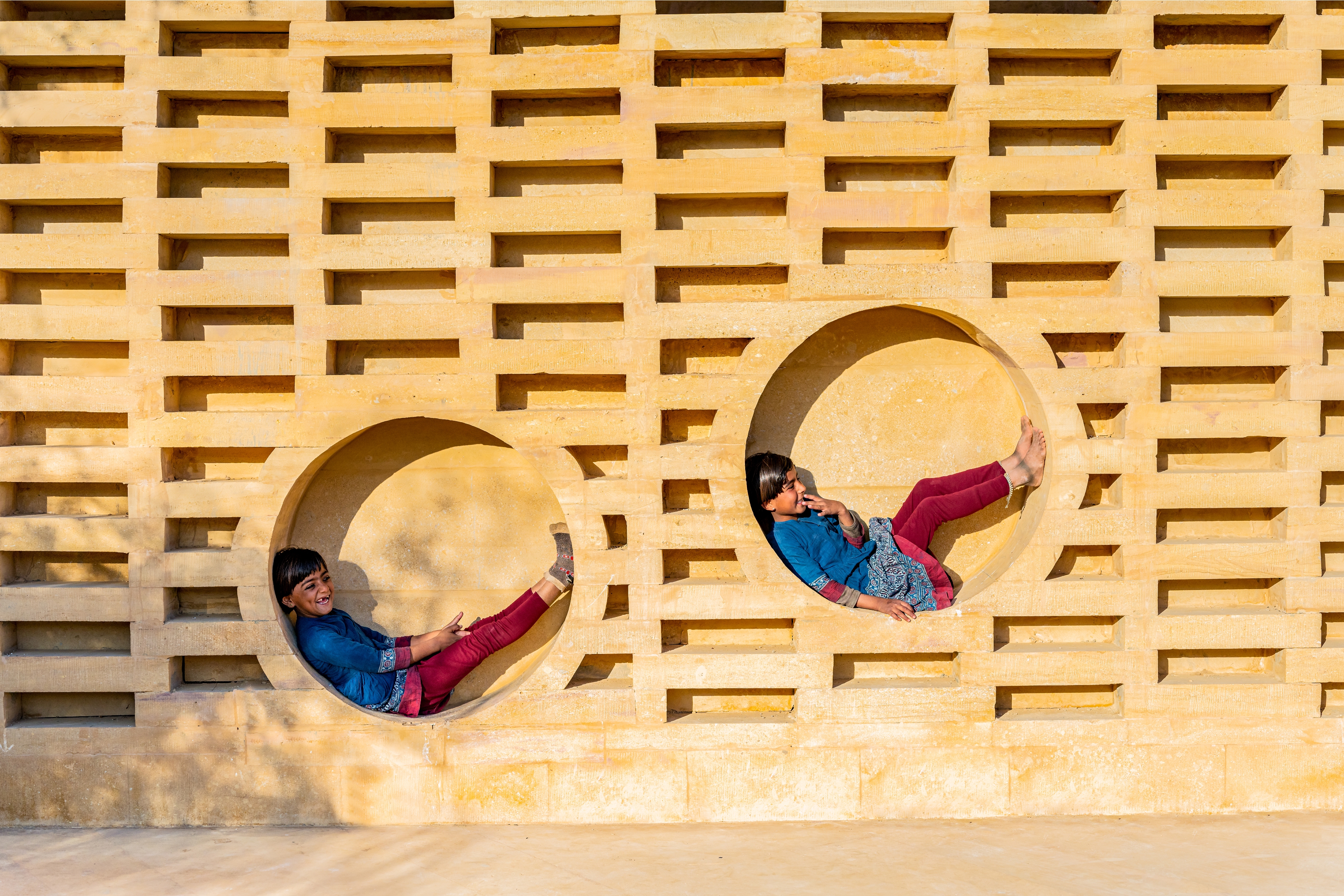 girls perching on the brick wall niches of the sustainable girl's school in India by Diana Kellogg