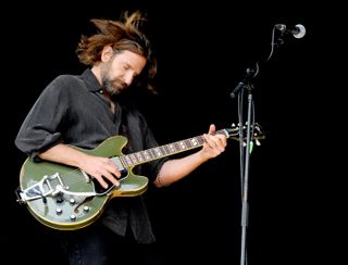 Bradley Cooper closes his eyes and throws his head forward as he plays guitar on stage.