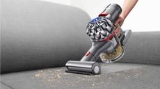 Dyson handheld vacuum cleaner cleaning up dirt from a sofa
