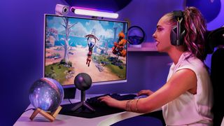 A streamer playing fortnite in a purple room. A logitech orb microphone and lite bar can be seen connected to the PC.
