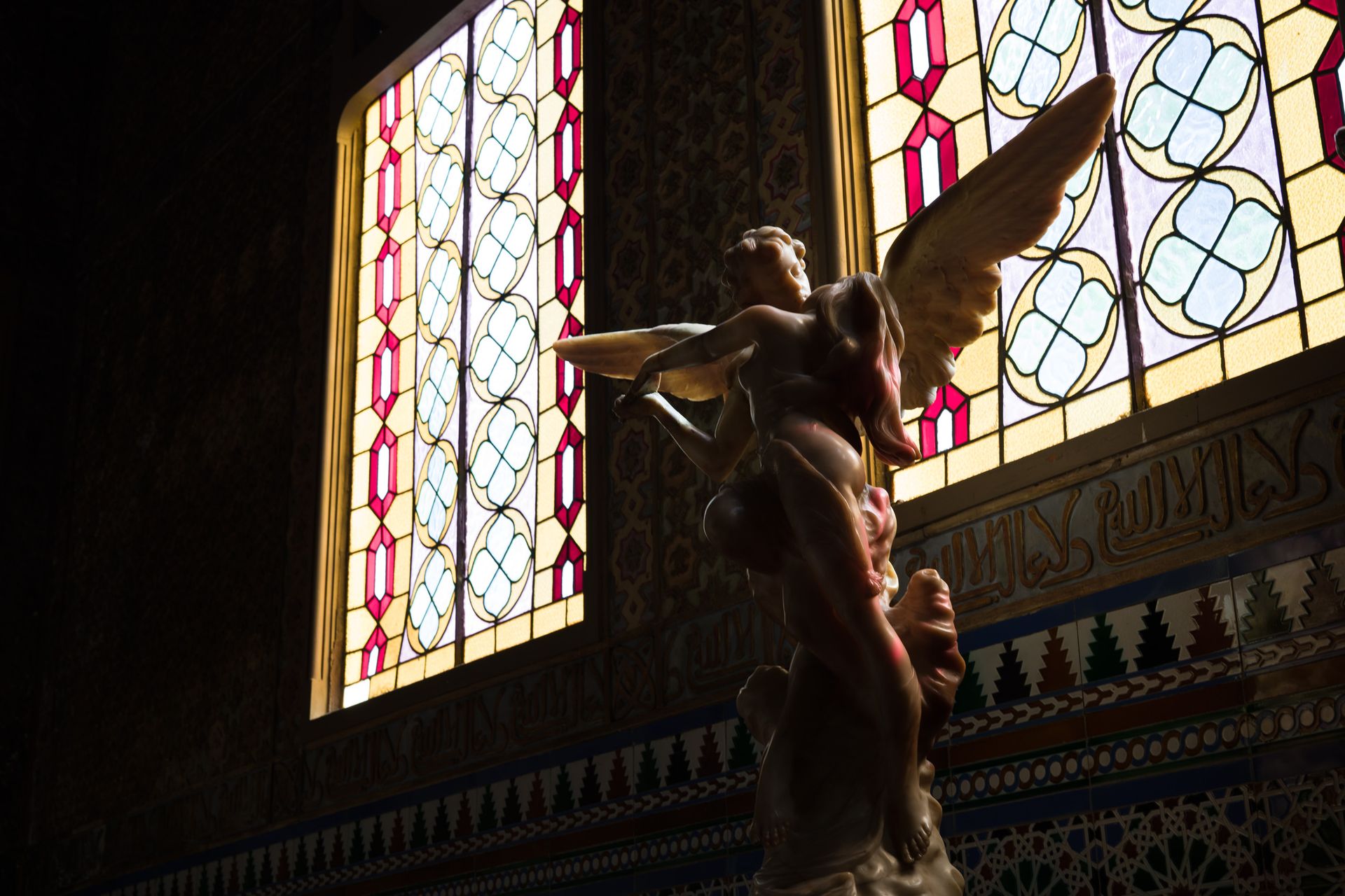  a statue of a cherub in front of bright stained glass windows