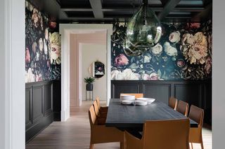 A dining room with a floral wallpaper and dark black wainscoting